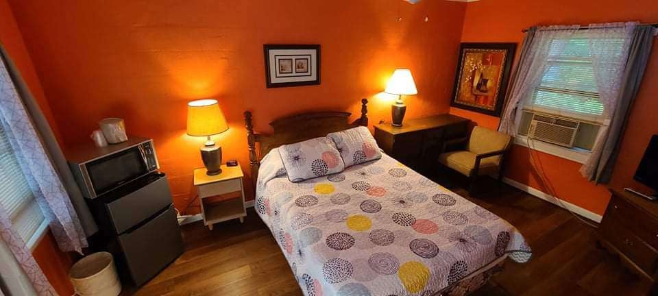 Warm-toned guest room with floral bedspread and window AC unit